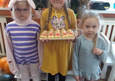 Trzy dziewczynki pozują do zdjęcia, jedna z nich trzyma ciastka